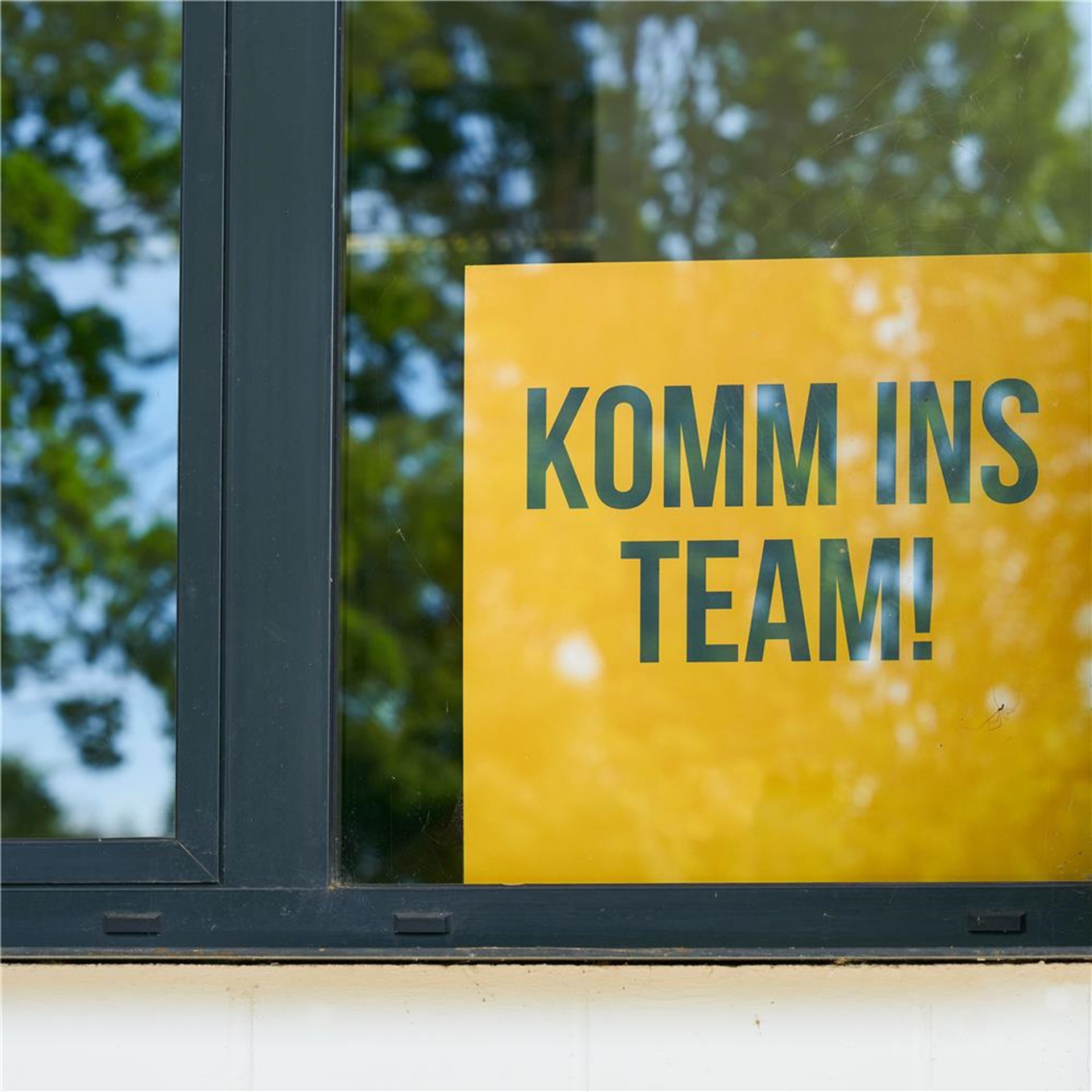 Komm-ins-Team Schild an einem Fenster